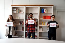 Drei Jugendliche stehen mit Abstand vor einem Bücherregal. Jeder hält ein Schild mit der Aufschrift "Abiprüfungen absagen" in roter Schrift in der Hand. Sie haben ernste Gesichtsausdrücke.