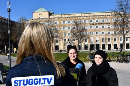 Man sieht zwei junge Frauen, die auf dem Schlossplatz stehen und interviewt werden. Das Mikrofon hält eine Frau, die von hinten zu sehen ist und deren Jacke die Aufschrift "STUGGI.TV" trägt.